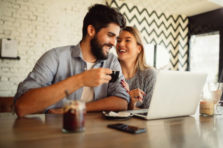 Young couple in cafeteria surfing the internet on laptop.